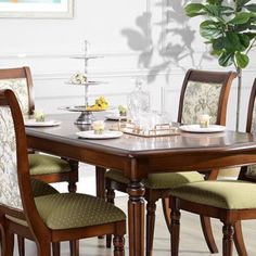 a dining room table with chairs and plates on it in front of a potted plant