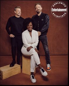 two men and a woman are posing for a photo in front of a brown background