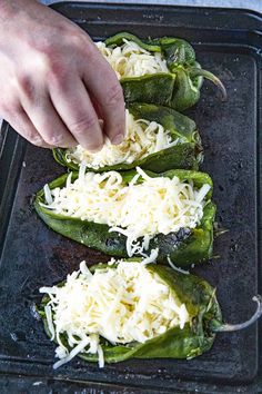 someone is sprinkling cheese on top of some green peppers in a baking pan