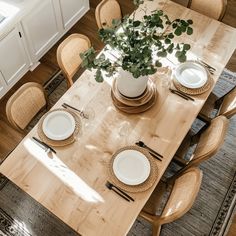 a wooden table topped with white plates and place settings next to a potted plant