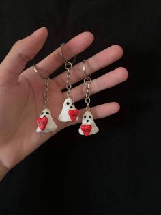 two white ghost key chains with red hearts hanging from them on a person's hand