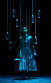 a woman standing in front of a bunch of glass bottles hanging from the ceiling,