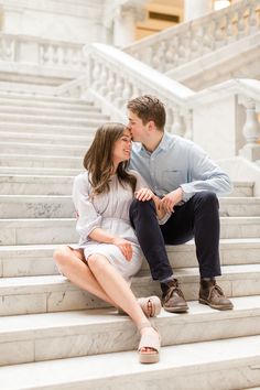 a man and woman sitting on the steps in front of some stairs with their hands around each other