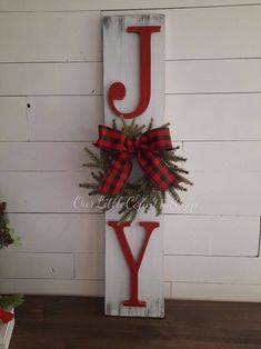 a wooden sign that says joy with a red bow on the letter j and evergreen branches