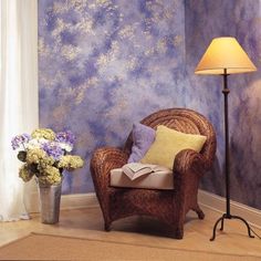 a chair and lamp in front of a blue wall with flowers on the floor next to it