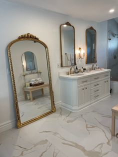 a bathroom with marble flooring and gold framed mirrors on the wall above the sink