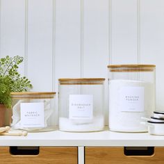 three glass jars with labels on them sitting on a shelf next to two planters