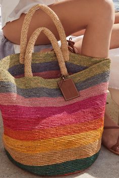 a woman sitting on the ground holding a multicolored bag