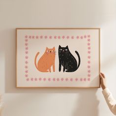 a person holding up a framed art print with two cats on it's side