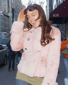 a woman walking down the street talking on her cell phone and wearing a pink jacket