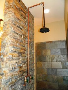 a bathroom with stone walls and exposed copper faucet, shower head and light fixture