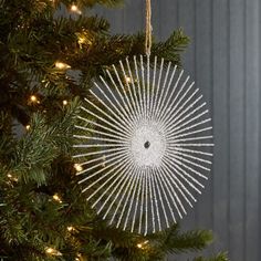 an ornament hanging from a christmas tree in front of a gray wall with lights