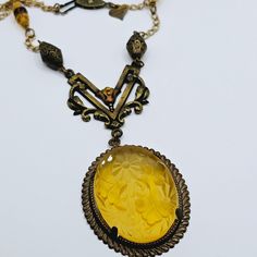 Lovely new old stock Victorian revival necklace by Glass Works Studio.  This is a very rare style. This wonderful piece features a large honey colored carved glass intaglio pendant surrounded by a bronze metal frame.  The intaglio glass has a lovely carved floral design.  The pendant is 4 inches long, including the decorative bale.  It is 1 3/8 inches wide.   The bale is very pretty with open work, enamel, and rhinestone accents.  The bale is made to look distressed. The necklace is 22 inches lo Collectible Yellow Gold Necklace With Antique Finish, Antique Yellow Jewelry Collectible, Antique Yellow Pendant Jewelry, Vintage Yellow Gold Intaglio Necklace, Antique Yellow Collectible Jewelry, Bronze Carved Collectible Jewelry, Victorian Yellow Jewelry Gift, Victorian Yellow Jewelry For Gifts, Collectible Carved Bronze Jewelry