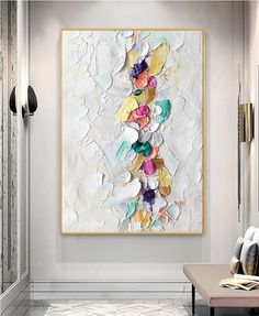 an abstract painting hangs on the wall above a bench in a room with white walls