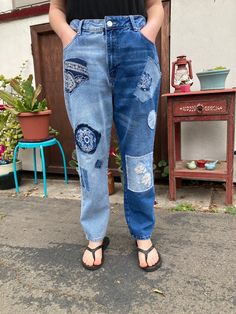 a woman standing in front of a door wearing blue jeans with patches on the side