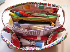 a purse filled with pens, markers and pencils sitting on top of a table