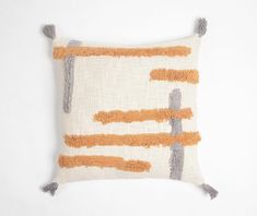 an orange and grey pillow with tassels on it's sides, against a white background