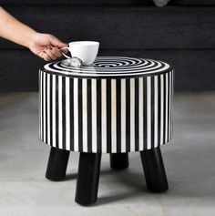 a person holding a coffee cup on top of a black and white striped stool with legs