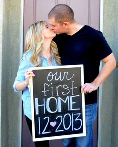 a man and woman kissing in front of a door holding a sign that says our first home 2012