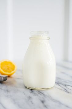 a glass jar filled with white liquid next to an orange slice on a marble counter