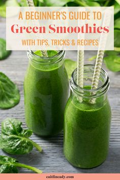 two mason jars filled with green smoothies on top of a wooden table next to spinach leaves