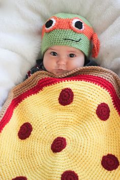 a baby wearing a crocheted hat and holding a blanket