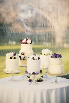 a table topped with three tiered cakes covered in white frosting and purple flowers