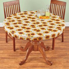 a wooden table topped with a white and yellow sunflower covered table cloth next to two chairs