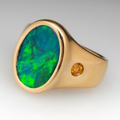 The satin finished ring is centered with a bezel set, oval, black opal cabochon. The shoulders are each flush set with one (1) round brilliant cut, fancy intense orange-yellow diamond. The ring measures 19.2mm at the top, rises 6.1mm above the finger, tapering to 5.4mm wide and 1.5mm thick at the base of the shank. We offer complimentary ring sizing to fit. Modern Oval Yellow Gold Opal Ring, Modern Yellow Gold Oval Opal Ring, Modern Oval Opal Ring In Yellow Gold, Modern Gold Oval Opal Ring, Modern Oval Opal Ring For Formal Occasions, Modern 14k Gold Oval Opal Ring, Oval Opal Ring With Bezel Setting For Formal Occasions, Luxury Oval Opal Ring With Bezel Setting, Modern Oval Opal Ring With Bezel Setting