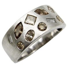 This beautiful 14k white brushed gold band is encrusted with diamonds of various shapes, sizes, and colors. The ring contains ten diamonds that include princess cut, round, square, tapered baguette, baguette, marquis, and moval shapes. The fancy colored diamonds range in shades of champagne, cognac, and chocolate—this combination of hues gives warmth to the ring and balances out the white gold. We love the composition of the diamond placement, which reminds us of confetti scattered across the ri Confetti Ring, Multi Band Ring, Sapphire Eternity Band, Ruby Bands, White Gold Sapphire, Gold And Silver Rings, Purple Band, Diamond Rings Bands, White Gold Band