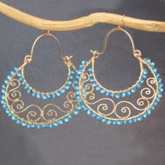 gold hoop earrings with blue beads and filigrees hanging from a tree branch