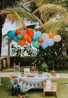 an outdoor party with balloons and desserts on the table in front of palm trees