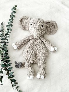 a crocheted stuffed elephant laying next to some green leaves on a white sheet