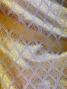 the sunlight is shining on a white and gold patterned material with intricate designs in it