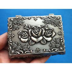 a small silver box with roses on the front and sides is held in someone's hand