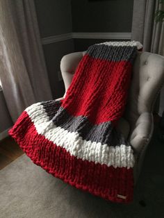 a red and gray blanket sitting on top of a white chair next to a window