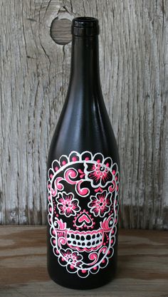 a black bottle with pink and white sugar skulls painted on the side sitting on a wooden table