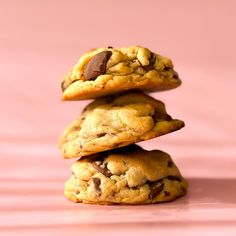 three chocolate chip cookies stacked on top of each other in front of a pink background