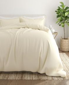 a bed with white sheets and pillows next to a potted plant on the floor