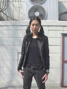 a woman standing on the sidewalk with her hands in her pockets and wearing black shoes