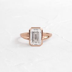 an emerald - cut diamond ring sits on a white surface