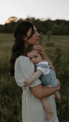 a woman holding a baby in her arms while standing in a field with tall grass