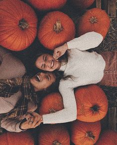 two people standing in the middle of a pile of pumpkins