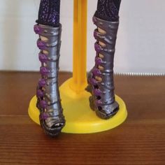 the legs and feet of a doll wearing purple shoes on a yellow stand with wood flooring