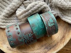 three different colored leather bracelets sitting on top of a wooden plate next to a gray sweater