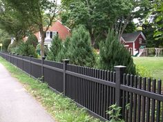 a black fence is next to a sidewalk in front of some trees and houses on the other side