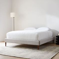 a white bed sitting on top of a wooden floor next to a lamp and rug