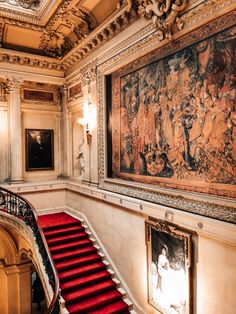 an ornate staircase with paintings on the wall and red carpeted steps leading up to it