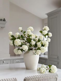 a white vase filled with flowers sitting on top of a kitchen counter next to a stool