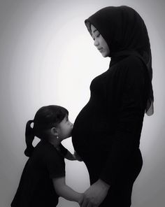 a black and white photo of a pregnant woman holding her child's hand as they both look at each other